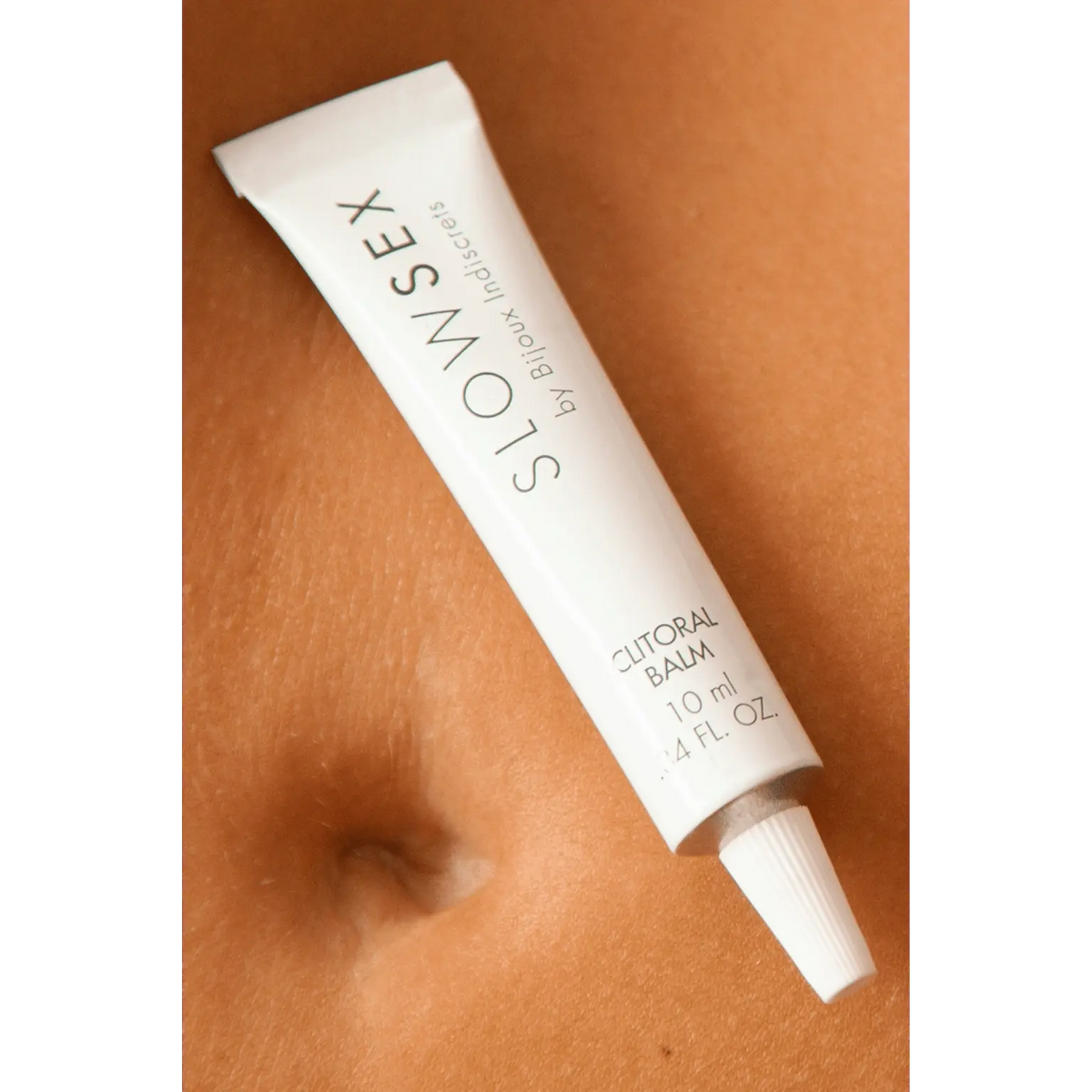 Baume chauffant clitoridien "Slow Sex" 10 ml de Bijoux Indiscrets posé sur le ventre, stimulant le plaisir féminin.