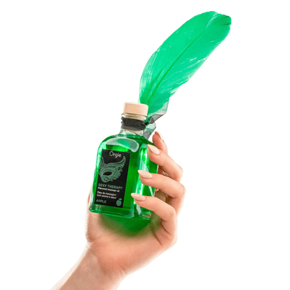 Huile de massage embrassable Sexy Therapy Pomme, de couleur verte, en bouteille avec un bouchon en liège, tenue dans une main avec une plume verte attachée au flacon.