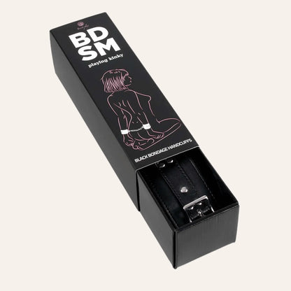 Emballage des menottes BDSM vegan en cuir noir, semi-ouvert, montrant le produit à l'intérieur avec une illustration discrète sur la boîte.