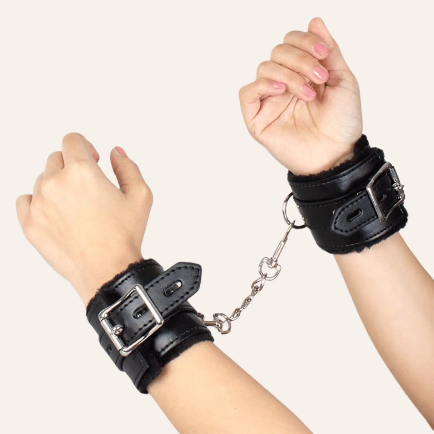 Menottes BDSM en cuir noir portées par une personne, avec une chaîne reliant les deux poignets, illustrant le confort et la robustesse des menottes.