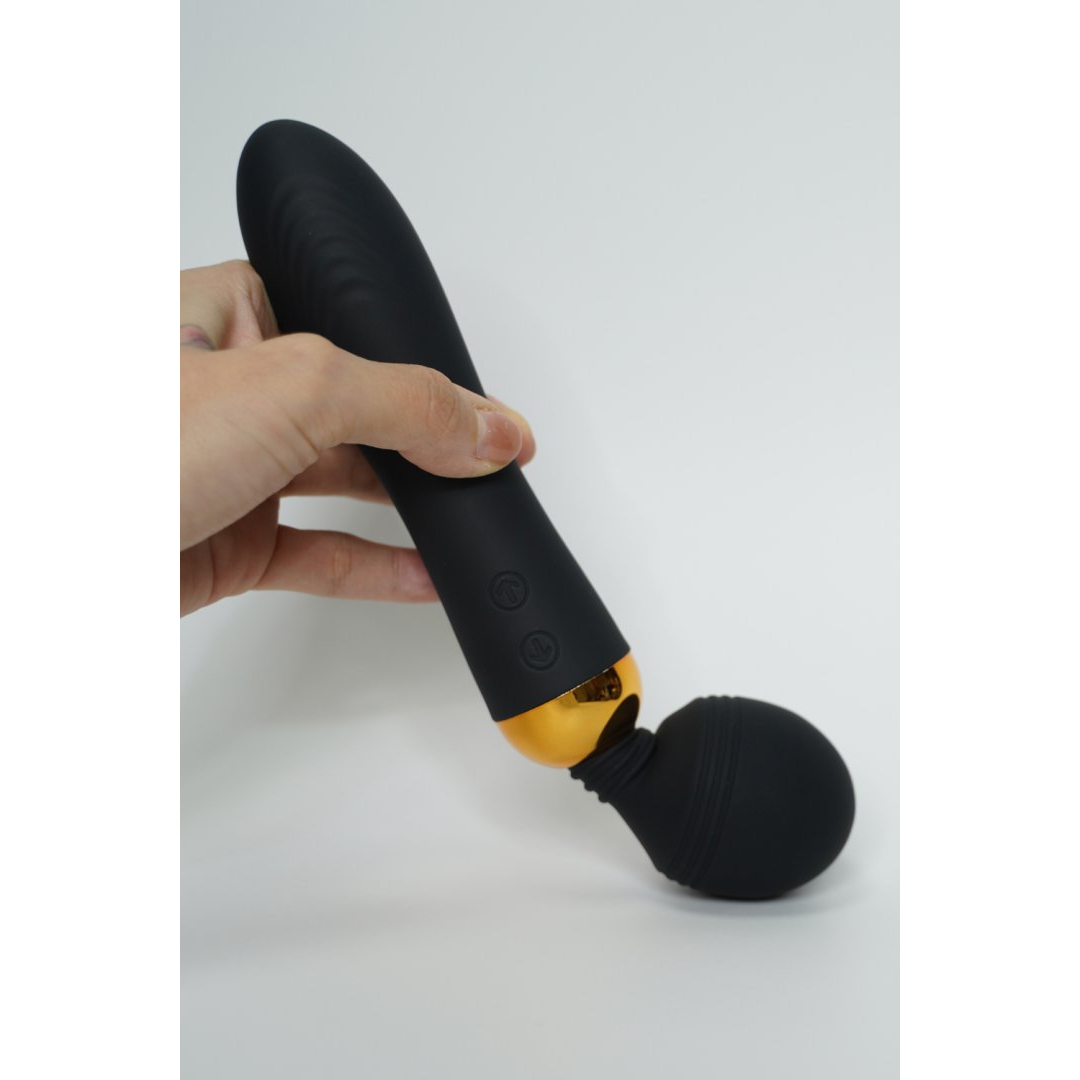 Main tenant le vibromasseur wand Shake noir en silicone, tete flexible pliee et anneau dore visible - Oh My God'Z
